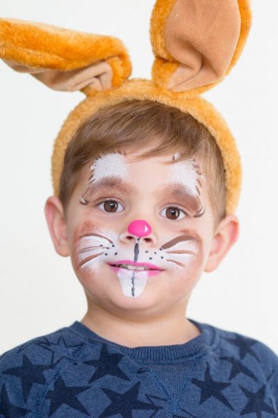 a boy wearing bunny face paint and tan bunny ears