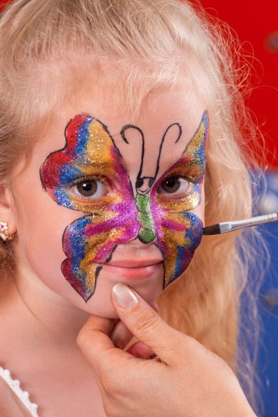 a young girl gets her face painted with a sparkly butterfly design